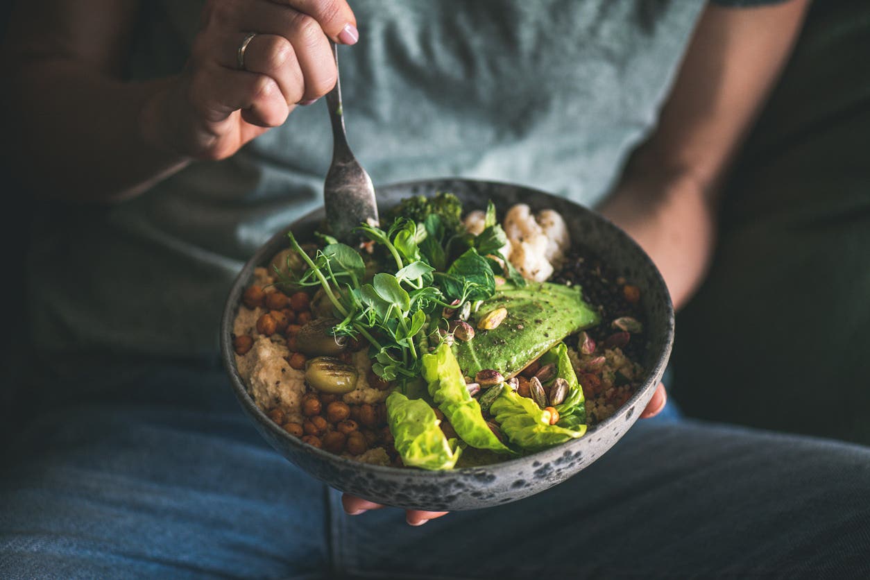bowl-of-fiber-rich-foods person eating a healthy vegan bowl meal featuring hummus, vegetable, salad, beans, couscous and avocado