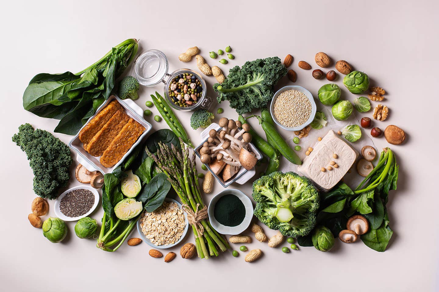 an-array-of-plant-based-sources-of-protein a wide array of protein-rich whole plant foods shown arranged on a white surface, including tofu, broccoli, tempeh, nuts, and seeds