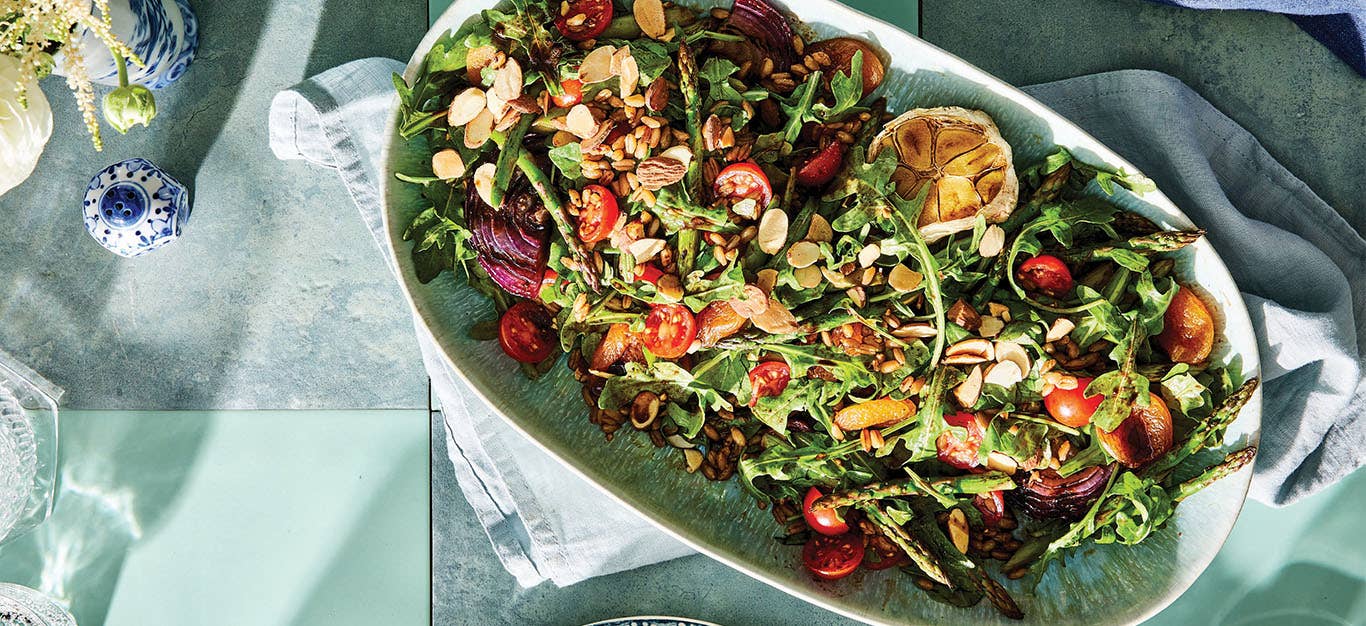 A large white platter of Grilled Asparagus Salad with Dried Apricots and Almonds on a table set with pale blue tablecloth and napkins