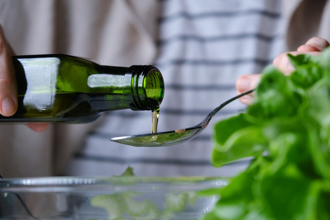 olive-oil Someone pouring olive oil into a spoon over a bowl of salad