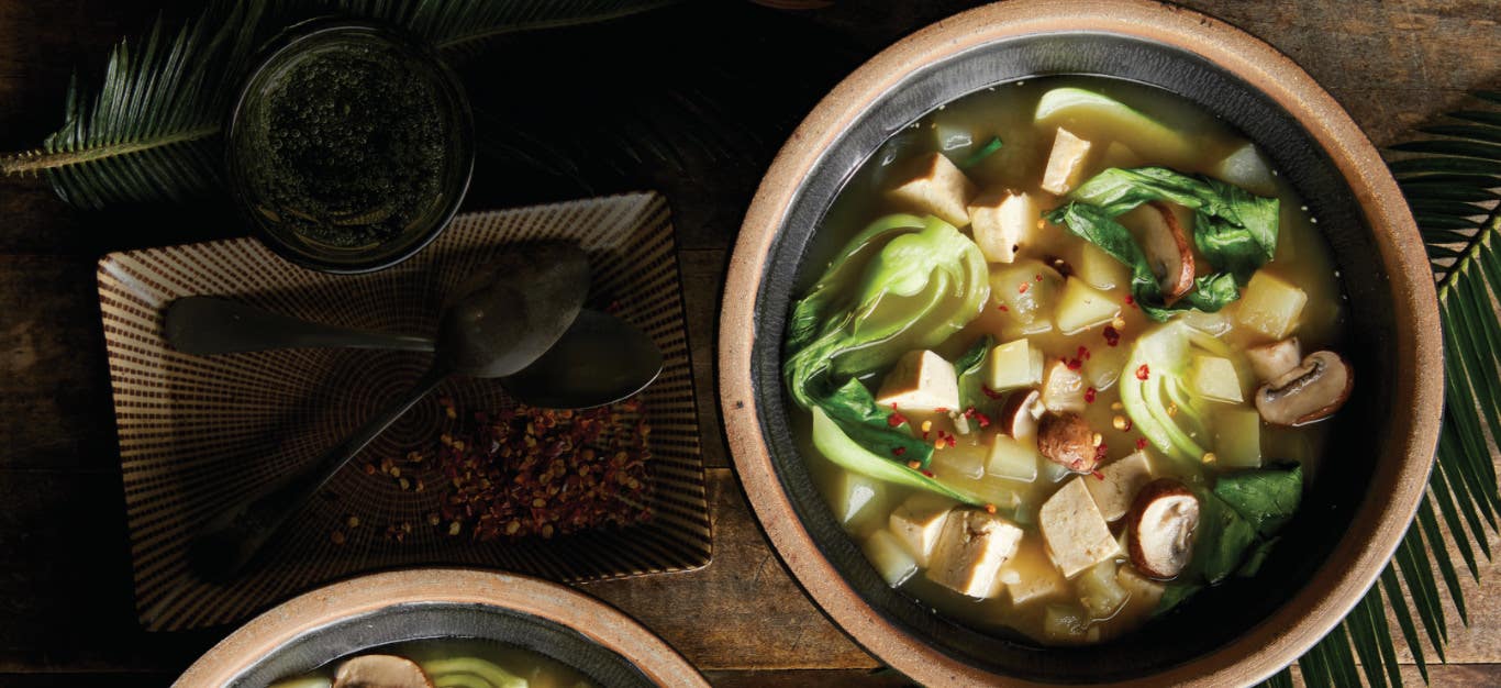A brown ceramic bowl of Tinola against in a dimly lit setting