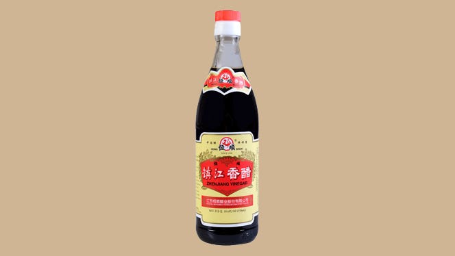 A bottle of Chinese black vinegar isolated on a tan background