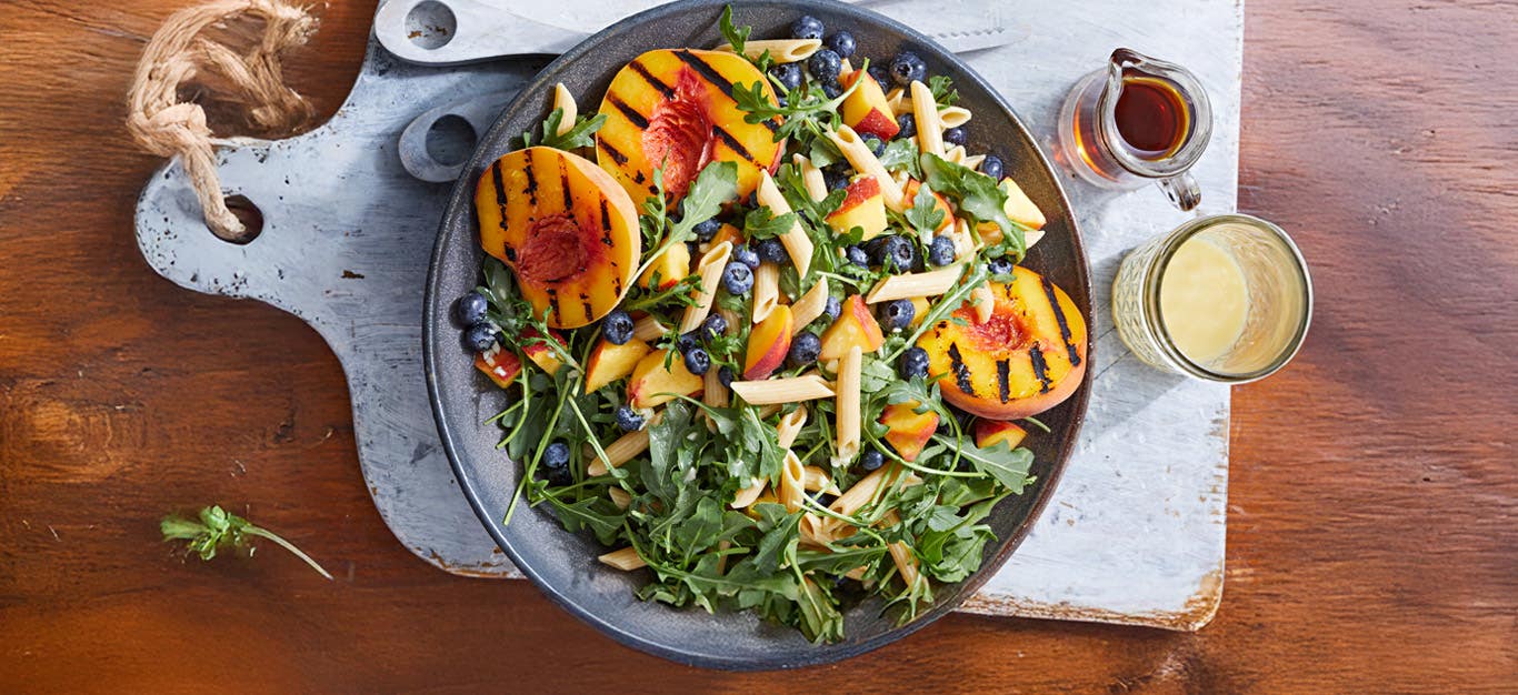 Arugula Peach Blueberry Salad in a bowl on a blue chopping board