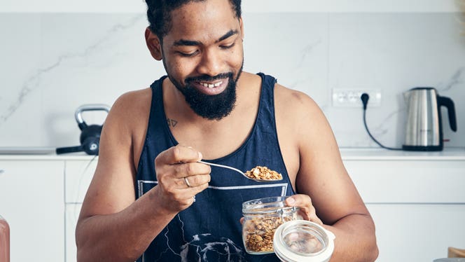 photo-for-athlete-protein-story A fit young man is in his kitchen happily spooning rolled oats into a bowl to make a healthy plant protein-rich meal